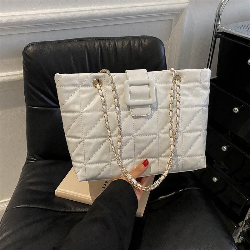 White Chanel-style quilted rhombus women shoulder bag with gold chain strap on black chair