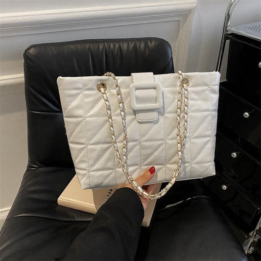 White Chanel-style quilted rhombus women shoulder bag with gold chain strap on black chair
