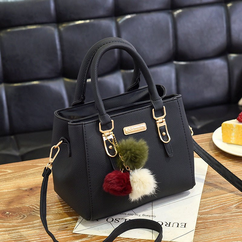 Black PU leather ladies handbag with plush tassel charm on wooden table