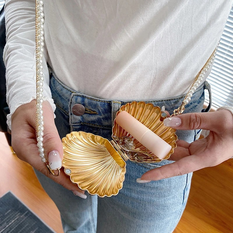 Gold shell-shaped mini purse crossbody bag holding a lipstick, featuring a pearl chain strap and car stitching design.