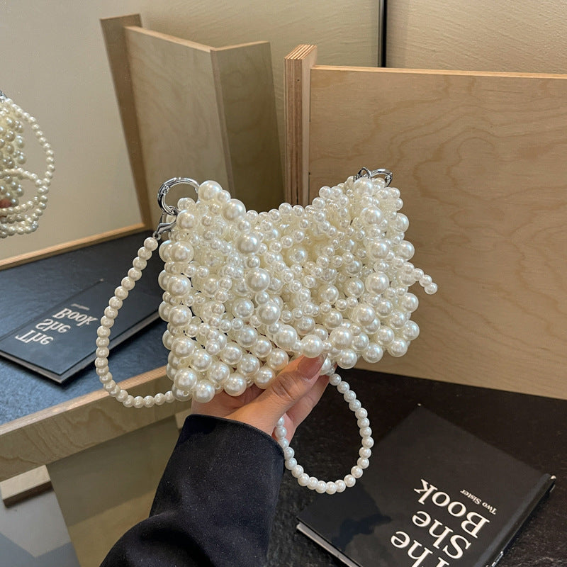 Woman holding creamy-white beaded pearl shoulder bag with bow detail on wooden background