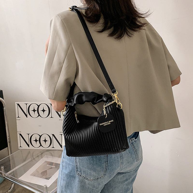 Black pleated PU leather women fashion crossbody bag with adjustable strap and gold hardware details worn with casual outfit