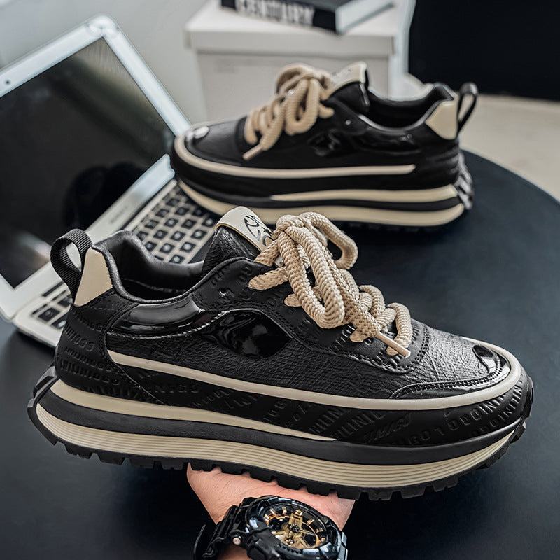 Black men's outdoor sneakers with thick beige soles and beige laces on a black table with a laptop in the background