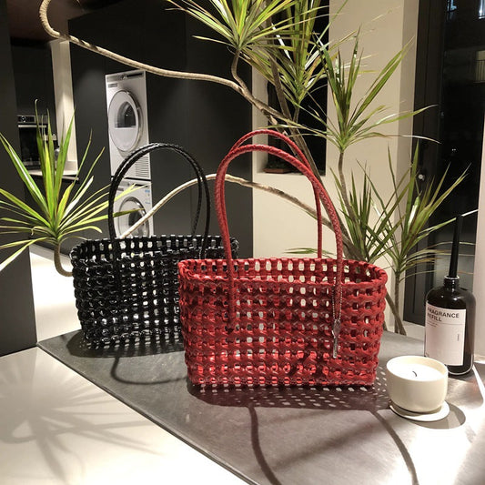 Two stylish Spot Hollow Woven Bags in red and black with a breathable, lightweight design placed on a countertop near plants and home decor items